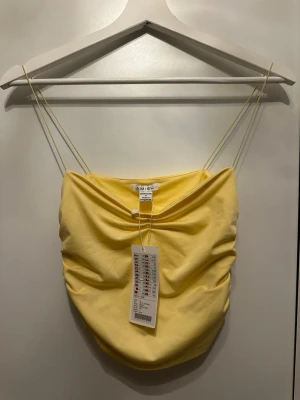 Gul linnetopp från Amisu - Trendig gul linnetopp från Amisu med tunna axelband och draperad front. Toppen har en croppad passform och är perfekt för varma dagar. Tillverkad i mjuk bomull som känns skön mot huden. Enkel men snygg design som passar till mycket.