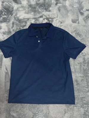 Marinblå pikétröja med krage -  marinblå pikétröja med klassisk krage och två knappar framtill. Tröjan har korta ärmar.       Perfekt för en avslappnad men ändå snygg look.