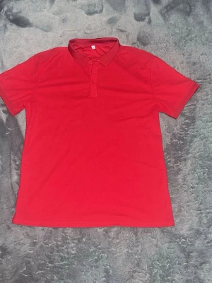 Röd piké t-shirt med krage - Snygg röd piké t-shirt med klassisk krage och knappar framtill. T-shirten har korta ärmar. Perfekt för en avslappnad och stilren look.