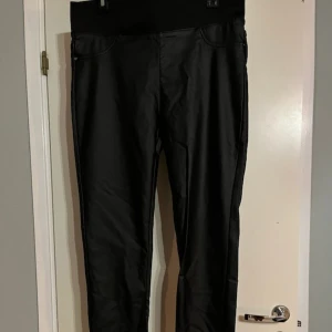 Svarta leggings med hög midja - Snygga svarta leggings med hög midja och diskreta fickor framtill. Materialet har en lätt glansig finish som ger en cool look. Perfekta att matcha med oversized tröjor eller crop tops. Passar dig som gillar en stilren och trendig outfit.