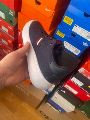 Marinblå Tommy Hilfiger sneakers - Snygga marinblå sneakers från Tommy Hilfiger med vit sula och diskret logga i rött, vitt och blått på sidan. Ovandelen är i textil med detaljer i syntetläder. Klassisk låg modell som passar till det mesta.