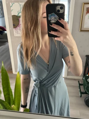 Ljusblå omlottklänning - Omlottklänning med knyt i midjan. Supermjukt material och endast använd 1 gång på ett bröllop men säljer pga fel storlek. Därav i superfint skick. 🩵