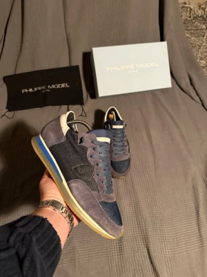 Philippe Model  - Snygga sneakers från Philippe Model i mörkblått och grått mocka och mesh. Skorna har vita och blå detaljer på sulan samt en ikonisk logga på sidan. Perfekta för dig som vill ha en stilren och trendig look.