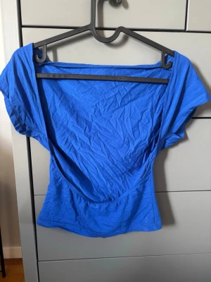 Blå öppen rygg topp - Snygg blå öppen rygg topp med korta ärmar. Toppen är figurnära och gjord i mjukt bomullsmaterial, perfekt för en trendig och avslappnad look. Enkel att matcha med både jeans och kjol.