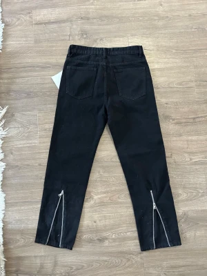 Svarta jeans med dragkedjor bak - Snygga svarta jeans med raka ben och dragkedjor längst ner på baksidan av benen. Klassisk femficksmodell och normal midja. Perfekta för en trendig och avslappnad stil. 