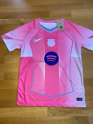 Rosa FC Barcelona matchtröja Nike - Snygg rosa FC Barcelona matchtröja från Nike med vita och blå detaljer. Tröjan har klubbmärke och Nike-logga på bröstet samt Spotify-logga i mitten. Tillverkad i lätt och ventilerande material, perfekt för träning eller match.