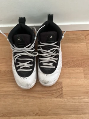 Vita och svarta Jordan sneakers - Säljer ett par vita och svarta Jordan sneakers med högt skaft och klassisk Jumpman-logga på plösen. Skorna har vita snören, svart mesh på ovandelen och detaljer i vitt läder. Perfekta för dig som gillar streetwear och sportig stil.
