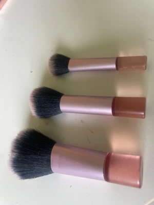 Set med tre sminkborstar i rosa - Ett set med tre sminkborstar med mjuka, täta borst i svart och ljusrosa. Handtagen är i metallicrosa med en matt rosa bas. Perfekta för applicering av puder, rouge eller bronzer. Snygg design som passar på sminkbordet.