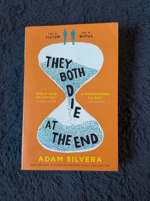 They Both Die at the End - En gripande ungdomsroman på engelska av Adam Silvera. Boken har ett orange mjukt omslag med ett timglasmotiv och svart text. Perfekt för dig som gillar känslosamma och tankeväckande berättelser om livet, vänskap och döden.