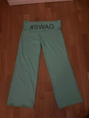 Mintgröna mjukisbyxor med #SWAG - Säljer ett par mintgröna mjukisbyxor med breda ben och hög midja. På linningen står det #SWAG i svart text. Byxorna är gjorda i ett mjukt och stretchigt material, perfekta för chill dagar eller när du vill ha en avslappnad stil.Om du intreserad jag vill bara förvarana att dom här byxorna är från en liten företag. Som hetter jennifer.