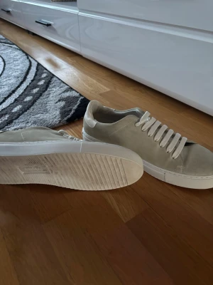 Beige sneakers från Axel Arigato - Snygga beige sneakers från Axel Arigato i mocka med vita snören och sula. Klassisk låg modell med stilren design som passar till det mesta. Perfekta för dig som gillar minimalistisk och clean stil. Använt kanske 2-3 gånger max 