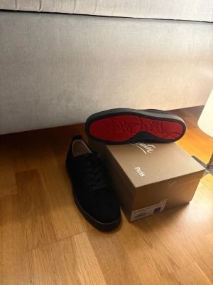 Svarta sneakers från Christian Louboutin - Snygga svarta sneakers från Christian Louboutin med klassisk röd sula och diskret logga. Skorna har en låg profil, svarta skosnören och är tillverkade i mocka. Perfekta för dig som vill ha en clean och exklusiv look.