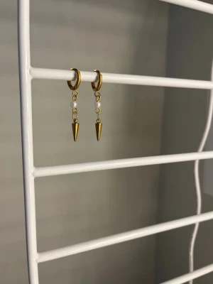 Guldiga hoops med pärldetalj och spets - Snygga små hoops i guldfärg med hängande spetsformad detalj och en liten vit pärla. Örhängena har minimalistisk design och passar perfekt för dig som gillar trendiga accessoarer med en edgy twist. Handgjort 