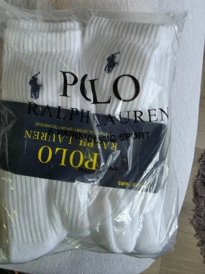 Vita sportstrumpor från Polo Ralph Lauren 6 par - Klassiska vita sportstrumpor från Polo Ralph Lauren med den ikoniska broderade loggan vid skaftet. Strumporna är ribbade och tillverkade i en mjuk bomullsblandning med polyester och spandex för extra komfort och stretch.