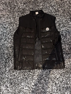 Moncler - Snygg svart dunväst från Moncler med quiltad design och dragkedja framtill. Där finns ett hål i ena fickan men de är inne i fickan så de syns inte och sömmarna på bilden har gått up på ena sidan men den sitter fortfarande fast. Pris går att diskutera 