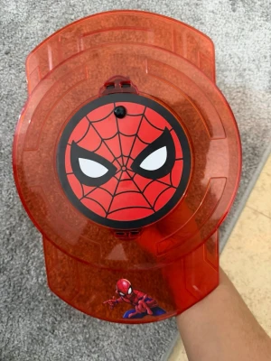 Spiderman leksaksset med sköld vattenpistol  - Säljer ett coolt Spiderman leksaksset med en röd plastsköld med Spidermans ansikte och en svart handhållen del. Perfekt för dig som gillar superhjältar och Marvel. Skölden har tydliga Spiderman-detaljer och är gjord i genomskinlig plast.Är också en vattenpistol 