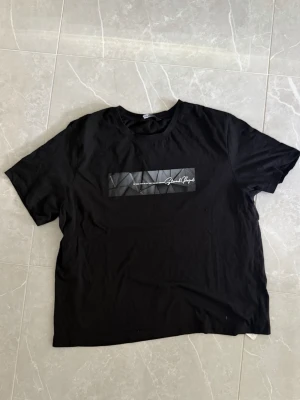 Svart t-shirt med tryck framtill - Snygg svart t-shirt med ett grafiskt tryck och text på bröstet. Klassisk rund halsringning och korta ärmar. Tillverkad i mjukt material som känns skönt mot huden. Perfekt till jeans eller shorts för en avslappnad look.