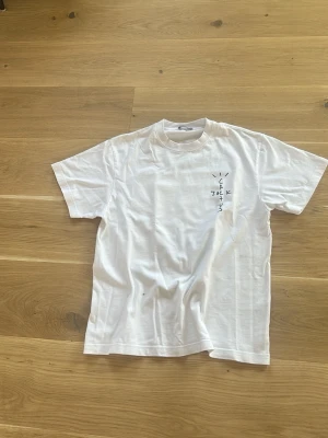 Vit Cactus Jack t-shirt - Säljer en vit t-shirt med tryck från Cactus Jack. Framsidan har ett diskret tryck på bröstet och baksidan har ett stort grafiskt tryck med texten 'LOOK MOM I CAN FLY' och en bild. Klassisk passform och rund hals.