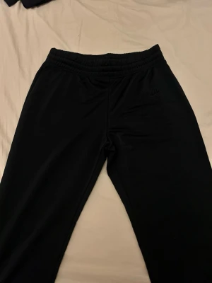Svarta mjukisbyxor från Nike - Säljer ett par svarta mjukisbyxor från Nike aldrig använt, med resår i midjan och dragsko för bästa passform. Byxorna har diskret Nike-logga på benet och är tillverkade i mjukt och bekvämt material. Perfekta för chill eller träning.