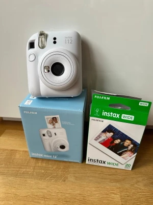 Fujifilm Instax Mini 12 vit kamera - Säljer en vit Fujifilm Instax Mini 12 direktbildskamera. Kameran har en rundad form och är tillverkad i plast. Medföljer originalkartong och ett paket Instax Wide film med 20 bilder. Perfekt för att ta roliga polaroidbilder direkt.