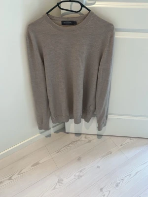 Beige merinoull tröja dressmann - En stilren beige tröja från Dressmann med rund halsringning och långa ärmar. Tröjan är tunnstickad och har ribbade muddar vid ärmslut och nederkant. Perfekt för lager på lager och enkel att matcha med olika outfits.