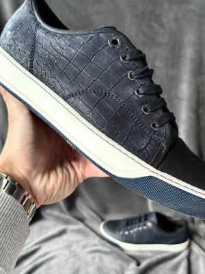 Blåa lanvins med reptilmönster - Snygga mörkblå sneakers med reptilmönstrad ovandel och svarta tåpartier. Skorna har vita sulor med blå kant och svarta skosnören. Materialet ser ut som konstläder med struktur. Perfekta för dig som vill sticka ut med en unik look. Storlek 41-42