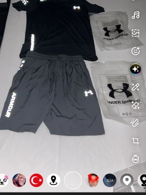 Svart träningsset från Under Armour - Säljer ett svart träningsset från Under Armour med t-shirt och shorts. Setet har reflekterande loggor och textdetaljer, samt elastisk midja på shortsen. Materialet är lätt och andas, perfekt för intensiva träningspass.