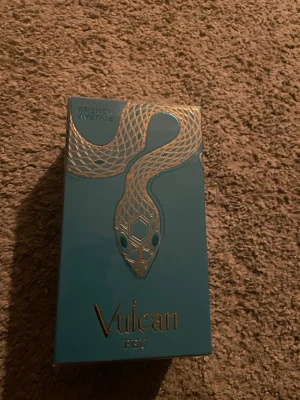 Vulcan Feu parfym med guldig orm - Parfymen Vulcan Feu från French Avenue kommer i en turkos box med en stilren guldig orm på framsidan. Förpackningen har en modern och exklusiv känsla med guldfärgade detaljer och text. Perfekt för dig som gillar unika och snygga designer.