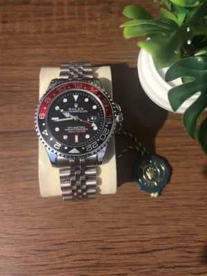 Klocka  - Snygg klocka med svart urtavla och röd/svart vridring. Klockan har en klassisk länk i silverfärgat stål och tydliga vita markeringar. Perfekt accessoar för dig som gillar exklusiv och tidlös stil. Priset kan diskuteras!