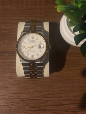 Klocka  - Snygg klocka med tvåtonad länk i silver och guld. Urtavlan är vit med gulddetaljer och datumvisning. Klockan har en räfflad guldfärgad bezel och klassisk design som passar till många stilar. Perfekt accessoar för dig som gillar exklusiva detaljer. Priset kan diskuteras!