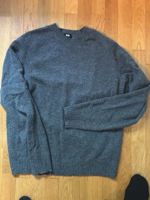 Grå stickad tröja från Uniqlo - Mysig grå stickad tröja från Uniqlo i klassisk modell. Tröjan har rund halsringning, ribbade muddar vid ärmslut och nederkant samt är tillverkad i mjukt material. Hör av dig vid funderingar!
