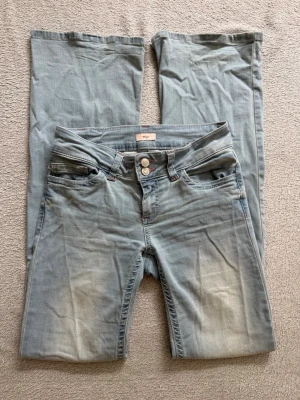Ljusblå bootcut jeans från nelly - Säljer ett par ljusblå bootcut jeans från nelly med dubbla knappar i midjan och rosa detaljer på fickorna. 