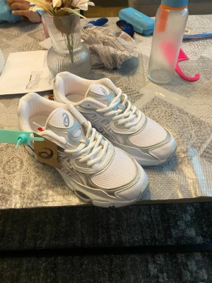 Vita Asics, den som köper för får skorna för 800 - Snygga vita Asics sneakers med detaljer i silver och grått. Ovandelen är i mesh och syntetmaterial för bra andningsförmåga och komfort. Klassisk snörning och chunky sula ger en sportig vibe. Perfekta för dig som gillar stilrena och bekväma skor.