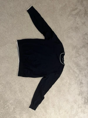 Mörkblå tröja från Nautica XL - Snygg mörkblå tröja från Nautica i storlek XL. Tröjan har vita detaljer vid halsringning, ärmslut och nederkant. Klassisk rund hals och lång ärm, perfekt för en stilren och enkel look.