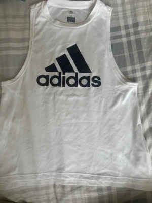 Vit Adidas linne  - Säljer ett vitt träningslinne från Adidas med stor svart logga på bröstet. Linnet är tillverkat i lätt och ventilerande Climalite-material som passar perfekt för träning och sportaktiviteter. Klassisk ärmlös design och rund hals. Defekt på sista bilden. Pris är diskuterbart. 