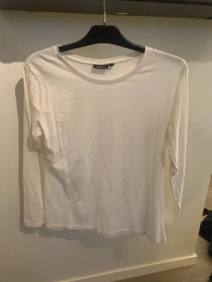 Vit långärmad topp - En enkel och stilren vit långärmad topp med rund halsringning. Perfekt att matcha med jeans eller kjol för en clean look.