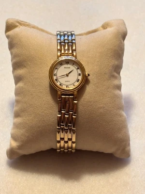 Guldfärgad klocka från Pulsar - Stilren guldfärgad klocka från Pulsar med klassisk rund urtavla och romerska siffror. Armbandet är i metall med en elegant länkdesign i guld och silver. Perfekt accessoar för dig som gillar tidlös och elegant stil.