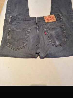 Grå Levi's raka jeans - Säljer ett par grå jeans från Levi's med klassisk femficksmodell och raka ben. Jeansen har en snygg tvättad look, Levi's ikoniska läderpatch bak i midjan och röda logotag på bakfickan. Materialet är slitstark denim i bomull. 
