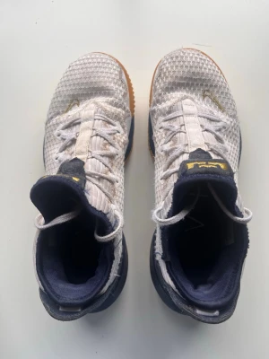 Lebron 16 olympic  - Snygga basketskor i vitt meshmaterial med mörkblå detaljer och gulddetaljer på plösen. Skorna har en unik sula i gummi med flera dämpande sektioner och en låg profil. Perfekta för dig som vill sticka ut på planen med både stil och komfort.priset är inte inristat i sten 