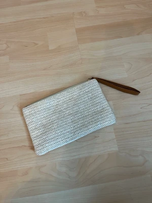 Beige kuvertväska i flätad look - Snygg beige kuvertväska med flätad struktur och dragkedja upptill. Aldrig använd.