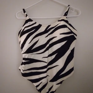 Zebramönstrad baddräkt från H&M. Strlk 44/Large. - Snygg baddräkt i nyskick från H&M med svartvitt zebramönster och smala axelband. Strlk 44/Large. Materialet är mjukt och stretchigt polyester, perfekt för strand eller pool. Modellen har en klassisk form med rundad hals och låg rygg. Supersnygg att matcha med solglasögon och strandväska. Felfri.