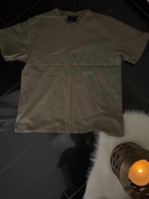 Beige t-shirt med tryck - Snygg beige t-shirt med diskret tryck i liknande ton på framsidan. T-shirten har klassisk passform och rund hals. Perfekt för en avslappnad och trendig stil.