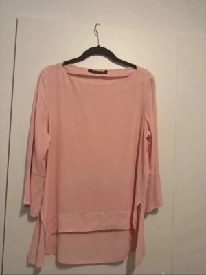 Ljusrosa blus med trekvartsärm - Ljusrosa blus med rund halsringning och trekvartsärmar. Blusen har en lös passform och slitsar på sidorna, vilket ger en avslappnad och trendig look. Materialet är tunt och lätt, perfekt för lager-på-lager. Passar dig som gillar stilrena plagg.