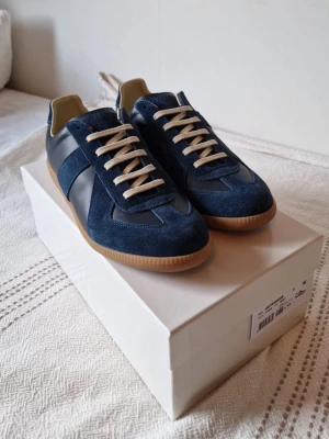 Maison Margiela GATS - Nu säljer jag ett par stilrena mörkblåa GATS i storlek 43, skicket är 9/10, boxen och dustbags ingår, skriv vid minsta lilla fundering och lägre pris vid snabbaffar.