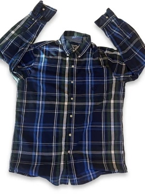 Rutig skjorta från Chaps (Easy Care) – Storlek M - Klassisk långärmad skjorta från märket Chaps i en snygg färgkombination av marinblått, grönt och vitt. Modellen är "Easy Care", vilket innebär att den är lättskött och kräver minimalt med strykning – perfekt för vardagen eller kontoret! • Märke: Chaps • Storlek: Medium (M) • Passform: Regular fit • Material: Bomullsblandning (Easy Care) • Skick: Mycket gott skick, inga hål eller fläckar. • Detaljer: Button down-krage och diskret broderad logotyp på bröstfickan. Jag skickar spårbart och snabbt! 