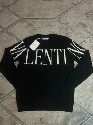 Svart stickad tröja från Valentino - Valentino Stickad Tröja - Vit/Svart Stickad tröja från Valentino i svart bas med vit logotyp över bröst och ärmar. Plagget är tillverkat i en finmaskig stickning som passar för sena sommarkvällar. 🌄🌆🏙️                                           OBS!: finns både S och M storlek