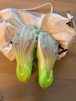 Adidas Adizero löparspikskor - Säljer ett par Adidas Adizero löparspikskor i neon-gult med svarta detaljer och vita sulor. Skorna har metallspikar under sulan för extra grepp på banan och är tillverkade i lätt syntetmaterial. Perfekta för sprint och friidrott. Endast testade på en träning. Sen valde barnet fotboll istället.