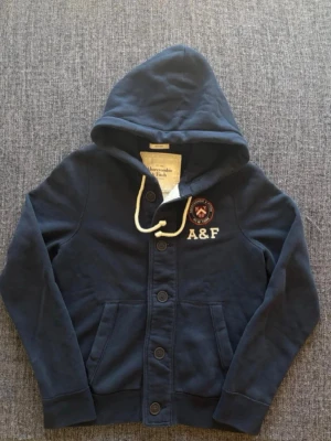 Abercrombie & Fitch hoodie strl M - En hoodie med knappar ifrån A & F i storlek M. Den är i mycket fint skick. Väldigt sällsynt och svår att få tag på. Hör av er vid frågor och funderingar!