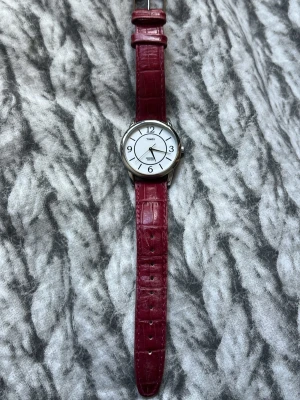 Timex klocka med rött läderband - Stilren klocka från Timex med ett vitt ur och tydliga svarta siffror. Klockan har ett klassiskt runt silverfärgat boett och ett rött läderband med krokopräglad struktur. Perfekt accessoar för dig som vill sticka ut lite extra.