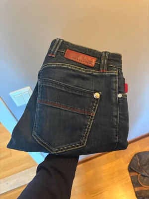 Mörkblå jeans från Tramarossa - Snygga mörkblå jeans från Tramarossa.med klassisk femficksdesign och kontrastsömmar. Jeansen har en rak passform och är tillverkade i slitstark denim med detaljer i rött och läderpatch bak i midjan. Perfekta för en trendig och avslappnad stil. Modell Leonardo